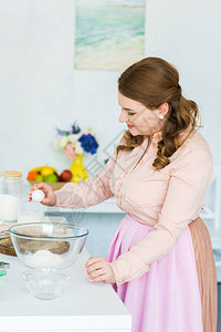 漂亮女人在厨房打鸡蛋做面团的侧视图图片