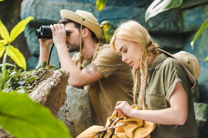活跃的年轻夫妇在游猎服和鹦鹉在丛图片