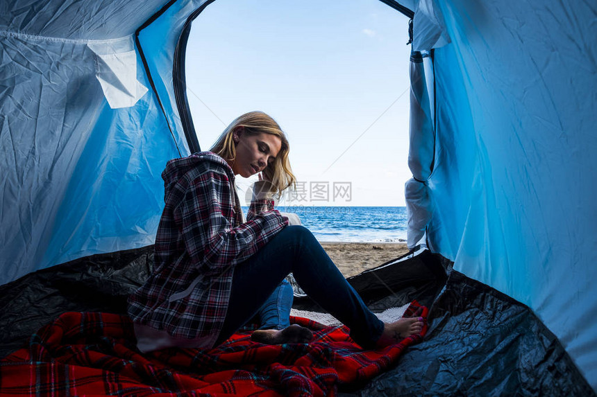 美丽的白种金发年轻女子在靠近海洋的海滩上的帐篷里过着另类的假期生活方式图片