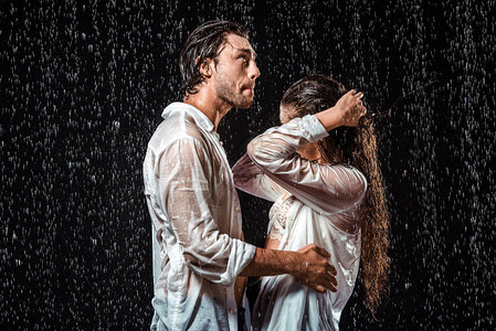 白色衬衫中的一对情侣的侧面站在雨下与图片