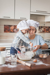 身戴厨师帽的年轻母亲和孩子在厨房杂乱的桌图片