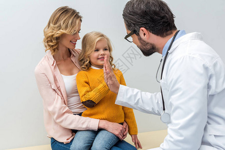 男儿童小儿科医生在小女孩坐在母亲膝上时图片