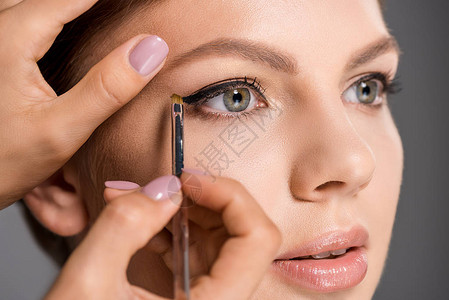 化妆师用眼线对模型灰色背景面部的图片