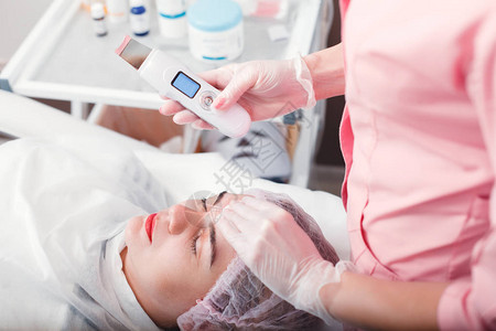 女青年在美容院接受温泉治疗医生持有超声波剪裁机斯帕疗法健图片