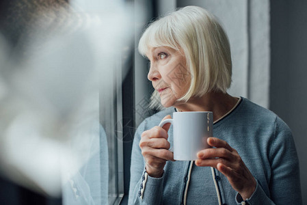 深思熟虑的老年女人在家里端着一杯咖啡背景图片