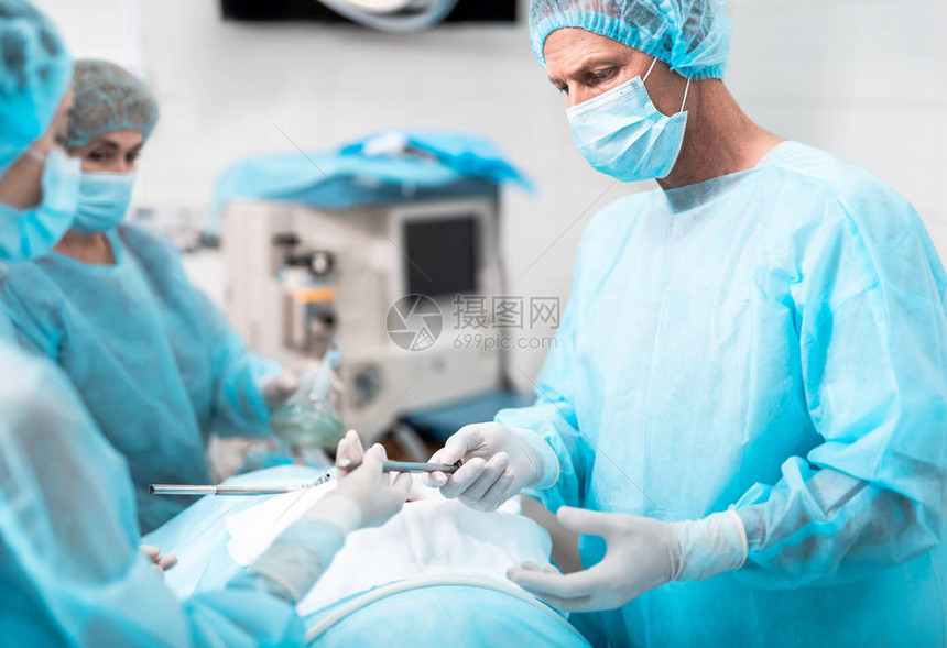 中年医生戴防护面罩手持腹腔镜工具站在手术室与图片