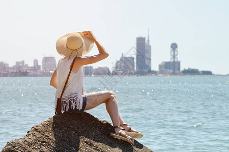 坐在海边岩石上的戴着帽子的女孩图片