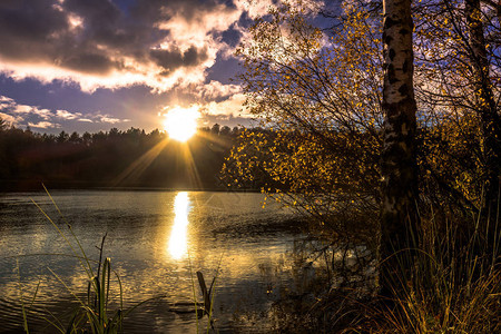 秋天的湖景色日落的天空和在森林上空的太阳光图片