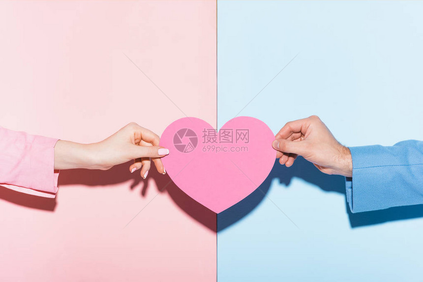 在粉红和蓝色背景上持有心形卡片的男子和妇图片