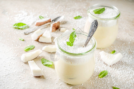 纯素甜食玻璃罐装椰子奶冻甜点椰子片和薄荷叶浅色混凝土石背景图片