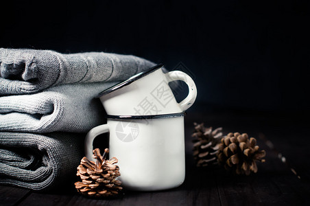 深色背景中的一堆灰色针织冬季毛衣搪瓷杯和冷杉球果背景图片