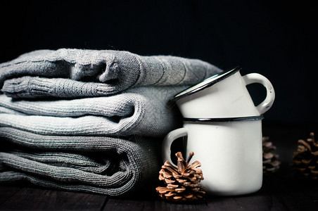 深色背景中的一堆灰色针织冬季毛衣搪瓷杯和冷杉球果背景图片