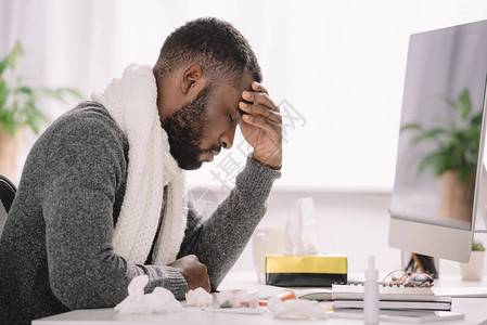 患有头痛坐办公室接受治疗和电脑的非洲累人男子背景图片
