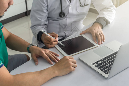 医生正在就他在医院使用技术平板电脑的办公桌上的健康状况咨询患者图片