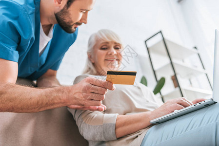持有信用卡并使用笔记本电脑看老年妇女的社工图片