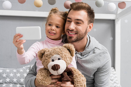 快乐的年轻父亲和女儿与泰迪熊Tedd图片
