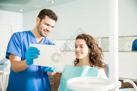 中成年牙医在牙科诊所治疗期间向女患者展示图片