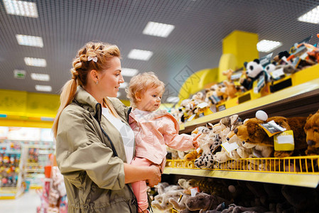母亲和她的小女孩在儿童商店中选择玩具图片
