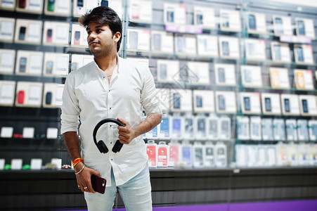 手机商店的印度男顾客买家用无线耳机连接到他的智能手机南亚人民和技术图片