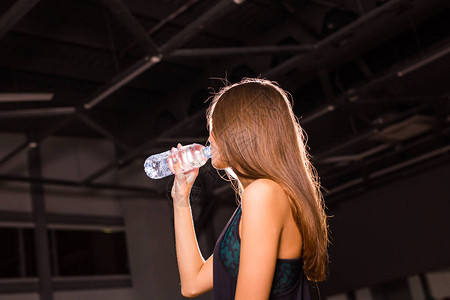 健身女人从瓶子里喝水在健身房休息的肌肉发背景图片