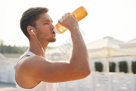 体育概念男子在海滩锻炼后喝水口渴的健康男与健康的身体喝清凉饮料跑步或户外训练背景图片