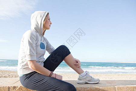 一位年轻体贴深思的女士坐在海滩旁图片
