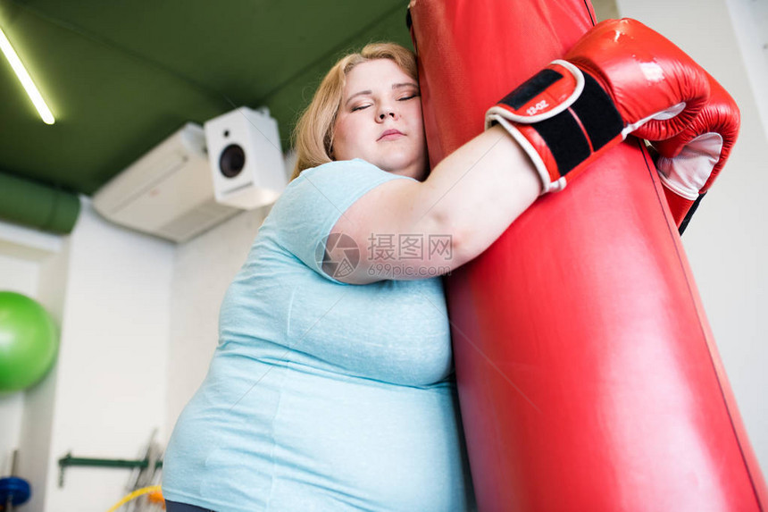 在健身房接受过极度减重训练后仰着拳袋闭着眼睛的胖女人图片
