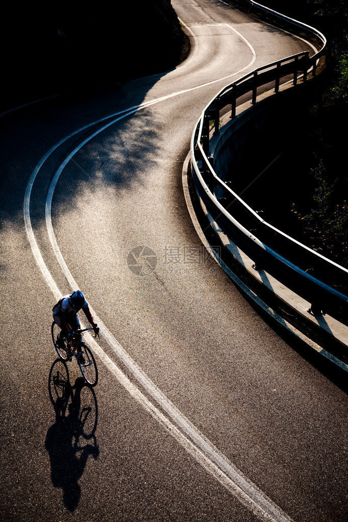 一名男骑自行车的人骑着公路自行车沿着铺好的山路骑行背图片