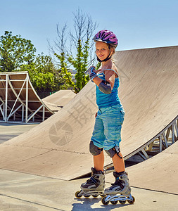 女孩溜冰鞋头盔步行公园孩子在滑板公园里骑着溜冰鞋初学者在公园学习轮滑背景图片