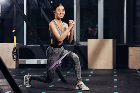 微笑的亚洲女孩在健身房用橡皮筋做弓步图片