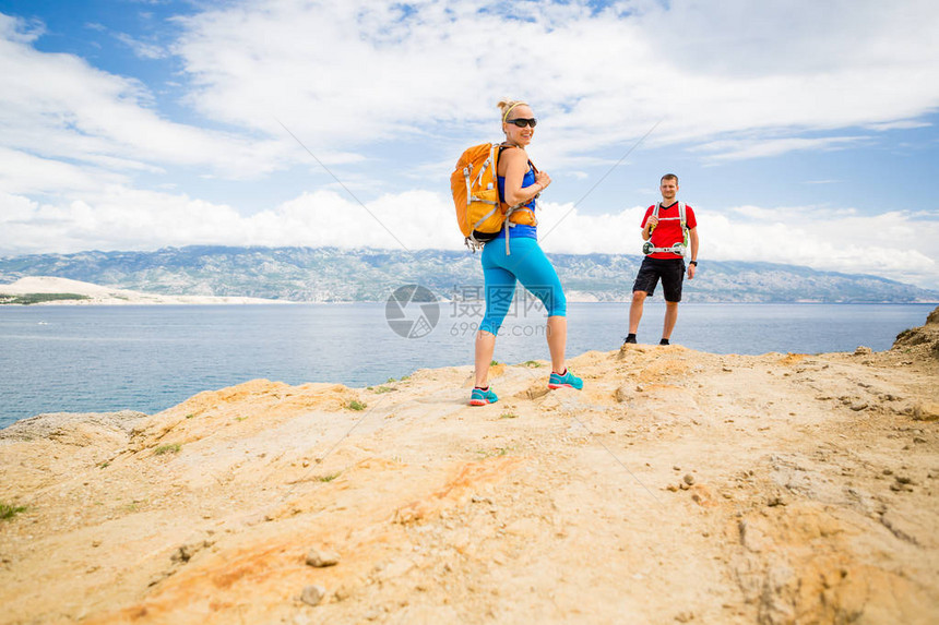 几个徒步旅行者在海边的小路上行走男人和女人在海边和山脉的夏季自然徒步旅行年轻夫妇在岩石山路上看着美丽的鼓图片