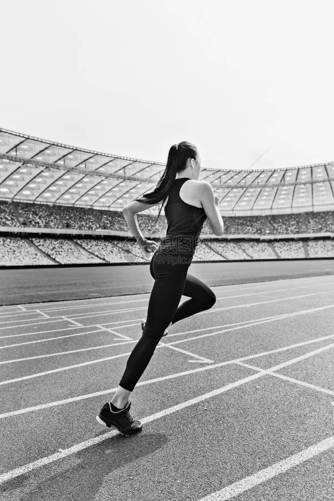 参加运动服的年轻健身女子在赛道体育场上跑图片