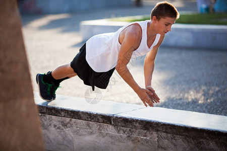 青年体育运动员在城市边境石上做俯卧撑城图片