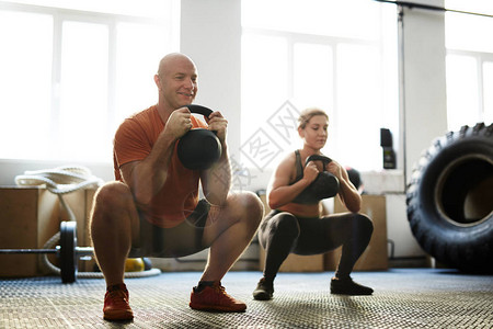 强壮的男人和女人在用壶铃锻炼时蹲着图片