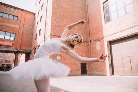 穿着白色芭蕾舞短裙在街上跳舞的年轻芭蕾舞演员的低视角图片