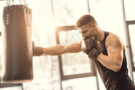在健身房用沙袋训练肌肉发达的年轻拳击手图片