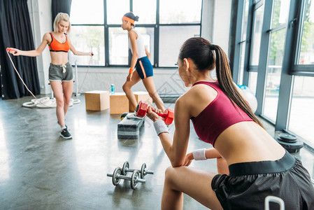 青年女运动员在健身场训练两名女运动员的同时背景图片