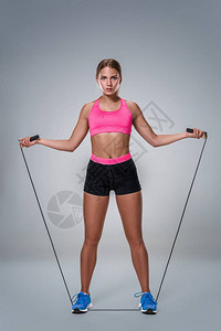 一个漂亮的健身女人在灰色背景下用跳绳锻炼的全长图像与美丽苗条健康的身体摆在工作背景图片