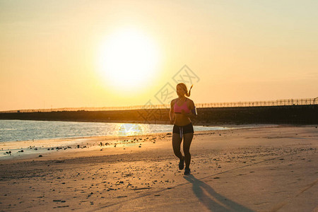 拥有智能手机的女运动员在沙滩上与阳光抗日跑步时使用臂背景图片