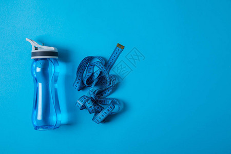运动瓶和测量胶带的顶部视图以蓝色最背景图片