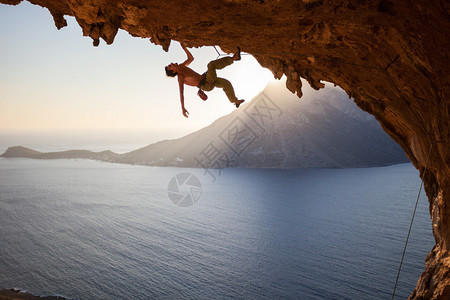 攀岩者在日落时沿着洞穴的屋顶攀爬背景图片