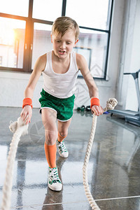 体育训练中可爱的男孩在健身工作室用绳子做运动服装训练图片