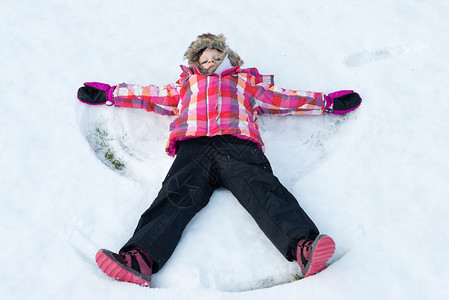 小女孩躺在雪地上制作雪天使孩子微笑着张开手脚图片