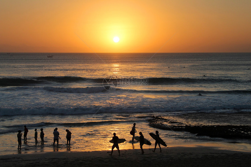 三个冲浪者剪影在红色日落的巴厘岛库塔海滩印度尼西亚图片