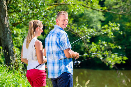 年轻夫妇在草丛中站在河岸边钓鱼或钓鱼图片