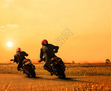 情侣朋友摩托车骑手在柏油公路上骑自行车对抗美丽的夕阳天空图片