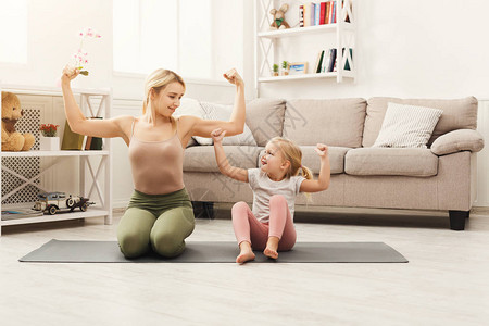 显示她的小女儿锻炼和肌肉的年轻母亲快乐的女孩在家训练母和的图片
