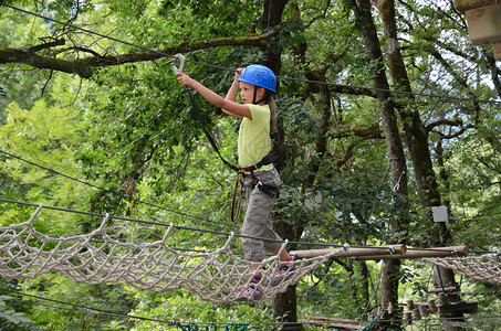 青春期前的女孩正在绳索课程的绳网上攀爬她在绿色森林图片