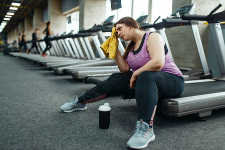 疲惫的超重女人坐在健身房的跑步机上图片
