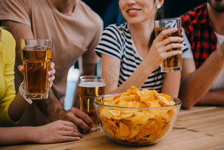 一群朋友在看足球比赛时坐在酒吧柜台旁的啤酒和薯片碗里图片